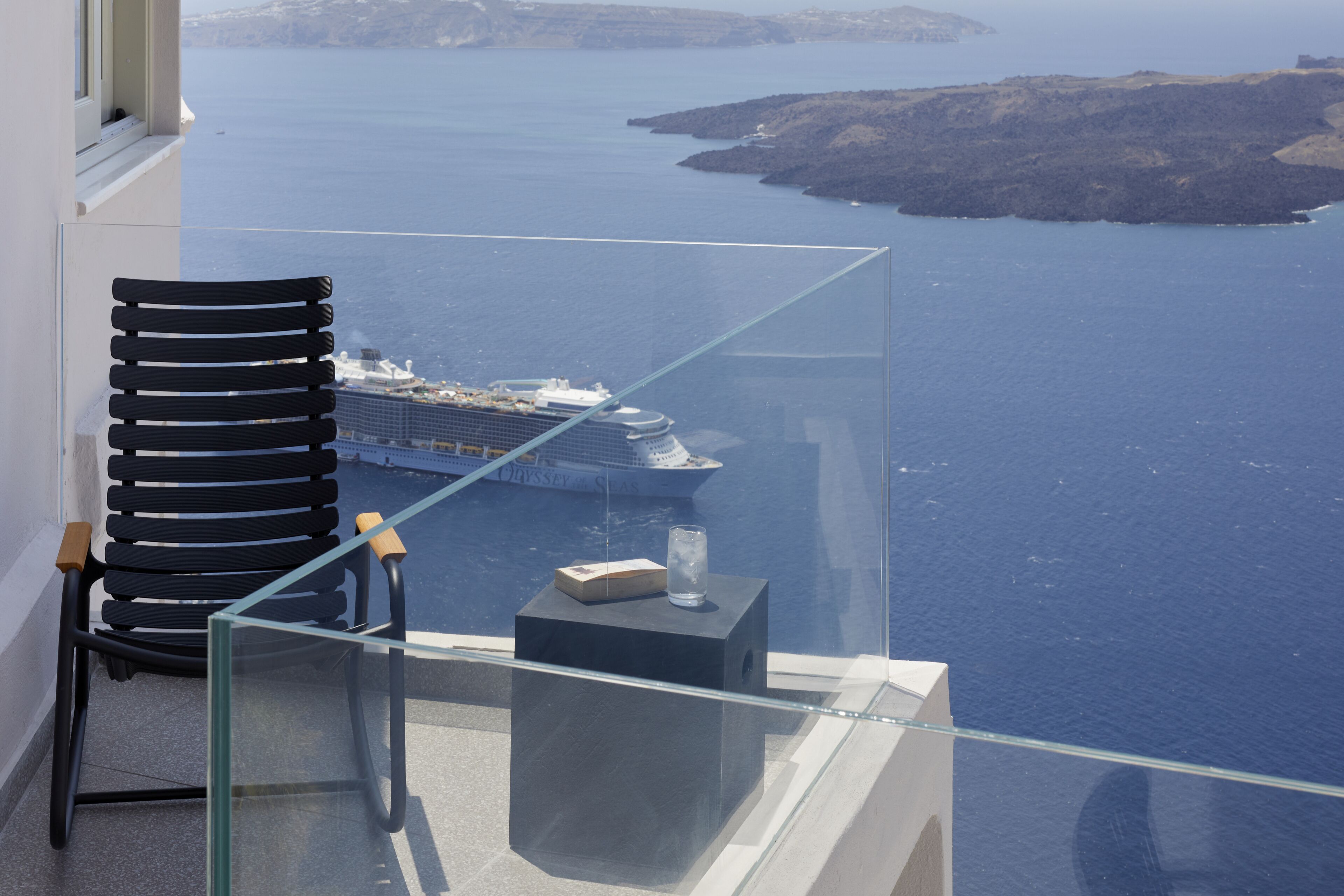 A balcony with a glass railing overlooking a body of water and a cruise ship.