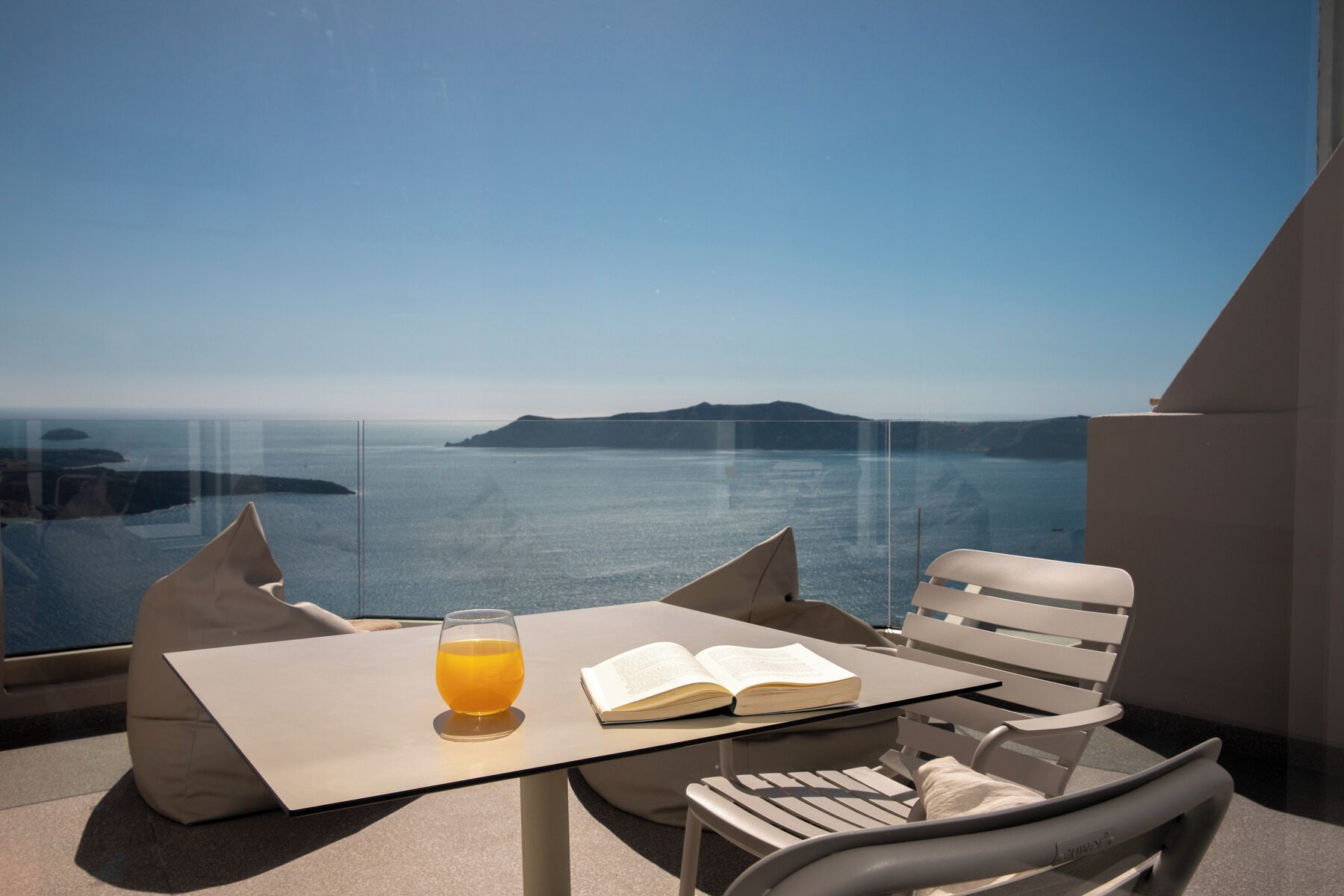 A balcony with a table, two chairs, a glass of orange juice, and an open book.