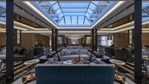 A spacious lobby with a high ceiling and skylight, featuring a central seating area with sofas and armchairs, surrounded by tables and decorative elements. - Batihan Beach Resort & Spa Ultra All Inclusive (Kusadasi)