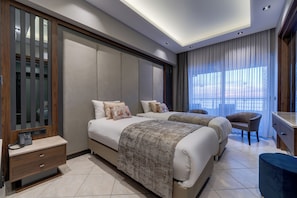 A modern hotel room with two beds, a desk, a chair, and a large window with curtains.