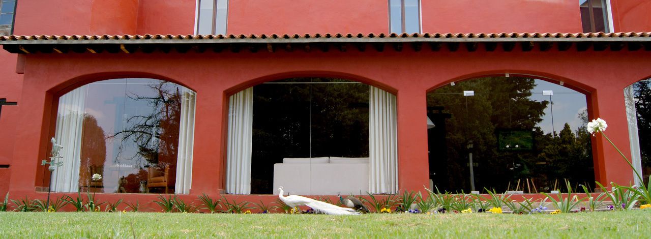 A red building with large arched windows and a white peacock statue in the garden.