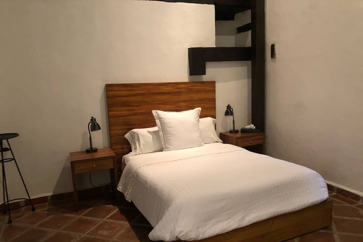 Una cama bien hecha con sábanas blancas, un cabecero de madera y dos mesitas de noche con lámparas.