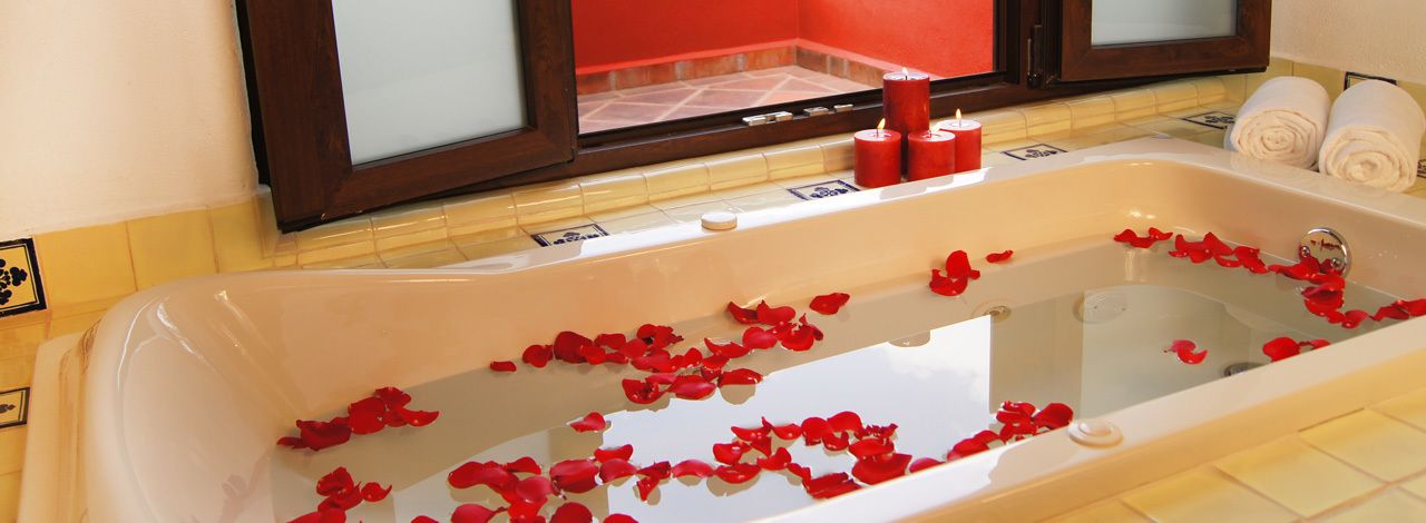 Una bañera llena de pétalos de rosa y velas, con toallas y un espejo al fondo.