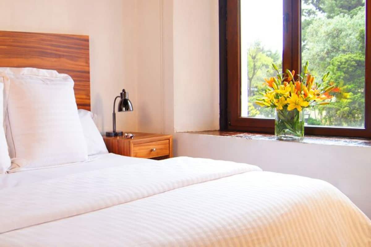 Una cama bien hecha con sábanas blancas, un cabecero de madera y dos mesitas de noche con lámparas.