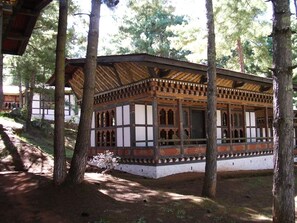 A traditional wooden structure with a balcony, surrounded by trees. - Olathang Hotel (Paro)