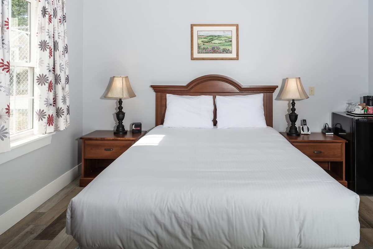 A hotel room with a large bed, two bedside tables with lamps, a framed picture on the wall, and a window with floral curtains.