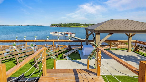 Una terraza de madera con un pabellón que da a un lago, filas de asientos y un muelle con barcos.