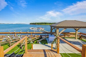 A wooden deck with a gazebo overlooking a lake, rows of seating, and a dock with boats.