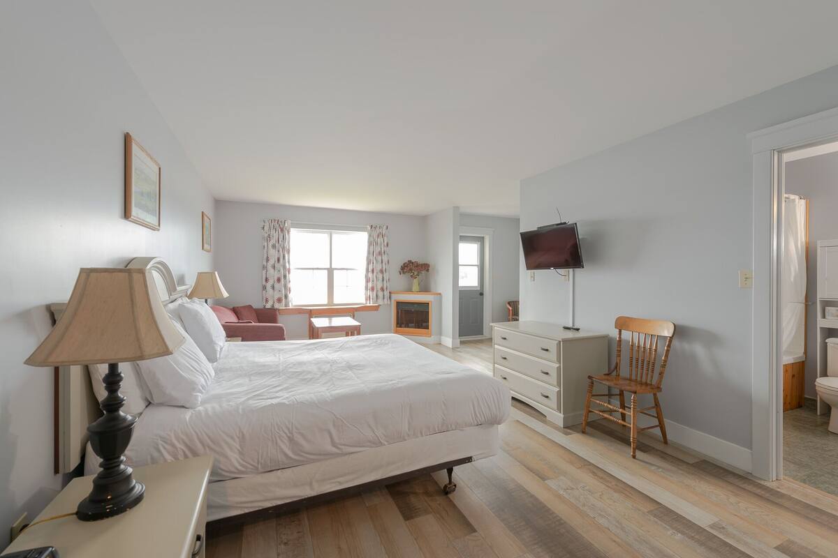 A bedroom with a bed, bedside lamps, a TV, a chair, and a small table.