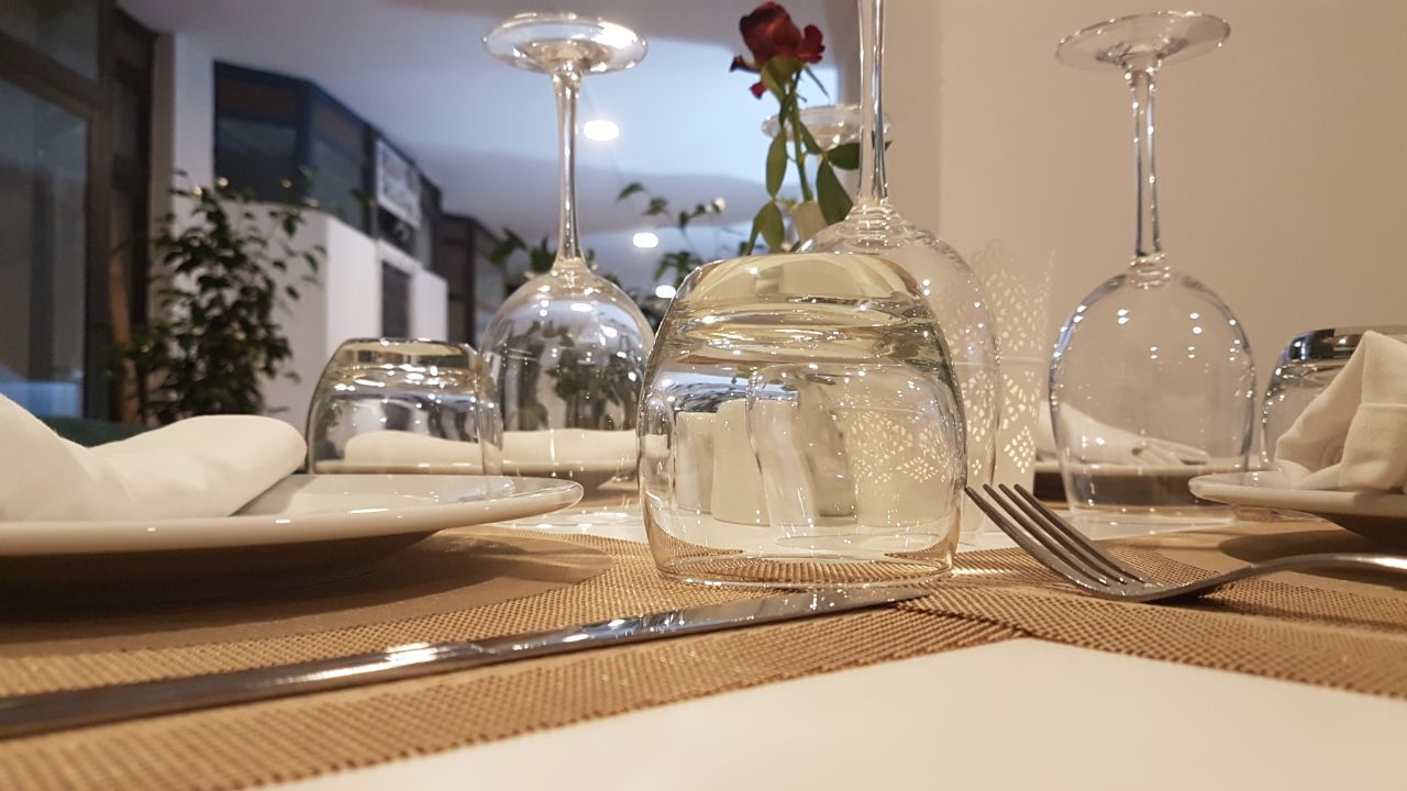 A table set with clear glassware, a vase with a single red rose, and a fork on a woven placemat.