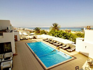 A rooftop pool with lounge chairs and a view of the sea.