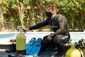 A person in a wetsuit sitting by a pool with scuba diving equipment. - Checkin Flamingo (Torroella de Montgrí)