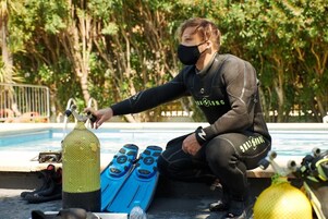 Una persona con traje de neopreno sentada junto a una piscina, con equipo de buceo.