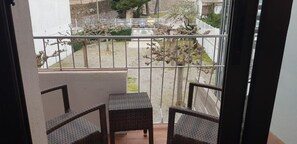 A balcony with two wicker chairs and a small table, overlooking a garden with trees and a fence. - Checkin Flamingo (Torroella de Montgrí)