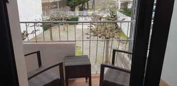 Un balcón con dos sillas de mimbre y una pequeña mesa, con vista a un jardín con árboles y una valla.