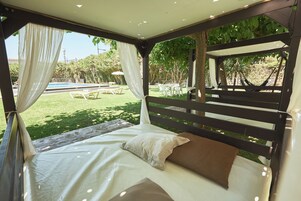 Una cama con dosel, vista a una piscina y mobiliario exterior.