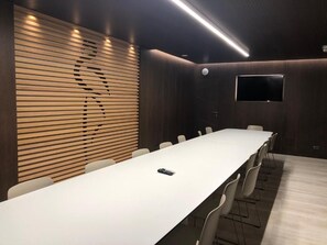 A conference room with a long table, chairs, a TV screen, and a wooden slat wall. - Checkin Flamingo (Torroella de Montgrí)