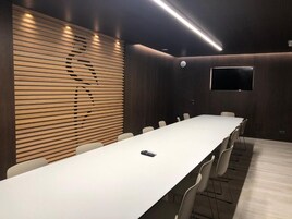 Un salón de conferencias con una mesa larga, sillas, una pantalla de televisión y un revestimiento de listones de madera.