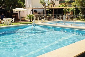 A clear swimming pool with a metal safety railing, surrounded by a covered seating area with white chairs and a table. - Checkin Flamingo (Torroella de Montgrí)