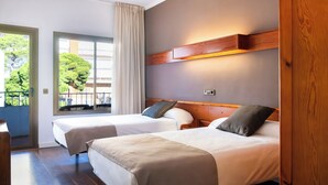 Hotellihuone, jossa on kaksi sänkyä, puinen pääty, ikkuna verhoilla ja näkymä vehreään maisemaan.