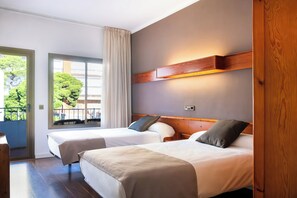 Habitación de hotel con dos camas, cabecera de madera, ventana con cortinas y vistas a zonas verdes.