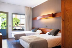 Habitación de hotel con dos camas, cabecera de madera, ventana con cortinas y vistas a zonas verdes.