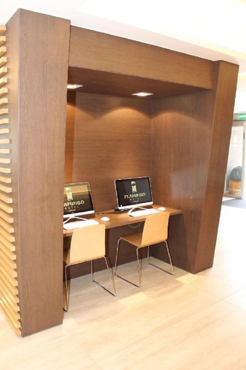 A wooden partition with two computer desks, each with a monitor displaying the Flamingo Hotel logo.