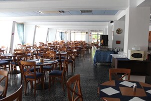 Un comedor amplio con varias mesas y sillas, un microondas y una mesa cubierta con mantel azul.
