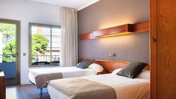 Habitación de hotel con dos camas, cabecera de madera, ventana con cortinas y vistas a zonas verdes.