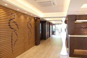 A modern hotel lobby with wooden paneling, a reception desk, and a clear pathway leading to the exit. - Checkin Flamingo (Torroella de Montgrí)