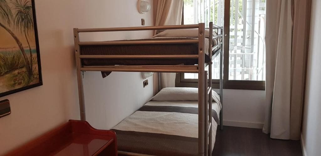 A bunk bed room with a window, a red chair, and a painting on the wall.