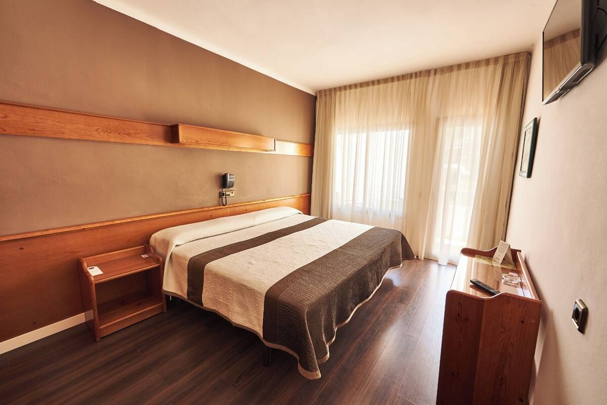 Ein Hotelzimmer mit einem hölzernen Bett, einem Nachttisch, einem Schreibtisch, einem Stuhl, einem Telefon und einem Spiegel.