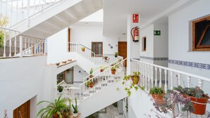 Un interior de varios niveles con paredes blancas, una escalera con barandillas y plantas en macetas.