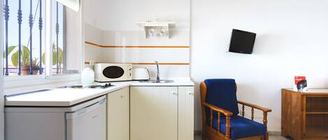 A compact kitchen with a microwave, sink, and white cabinets. There's a wooden chair and a small wooden table.