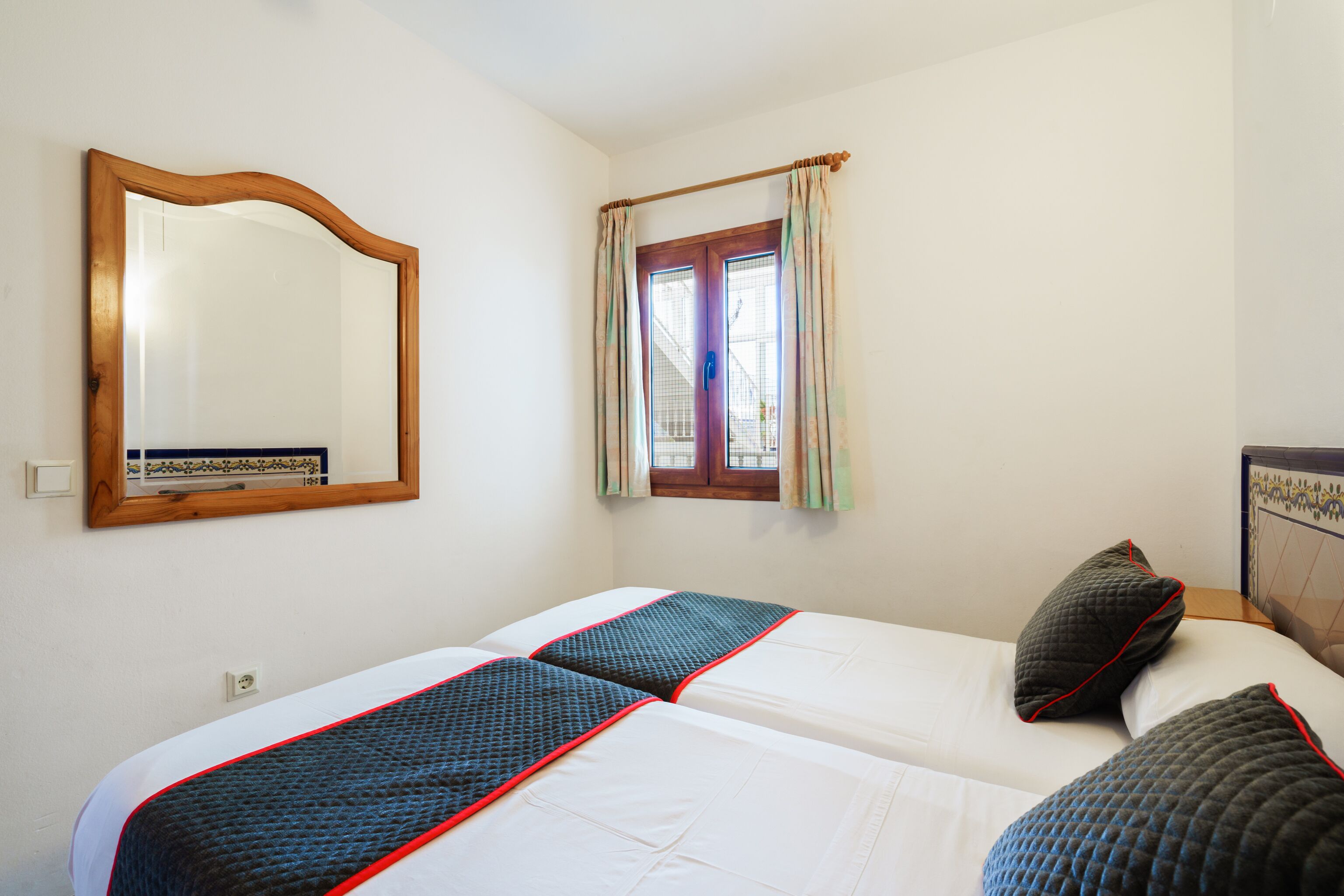 Una habitación con dos camas, un espejo de madera y una ventana con cortinas.