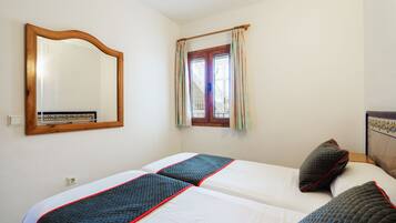 Una habitación con dos camas, un espejo de madera y una ventana con cortinas.