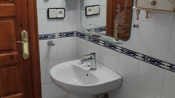 A bathroom with a wooden door, a white sink with a mirror above it, a toilet, and a glass shelf with toiletries.