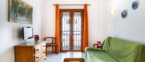 Una habitación con un aparador de madera, un sofá verde, una mesa de madera y una ventana con cortinas naranjas.