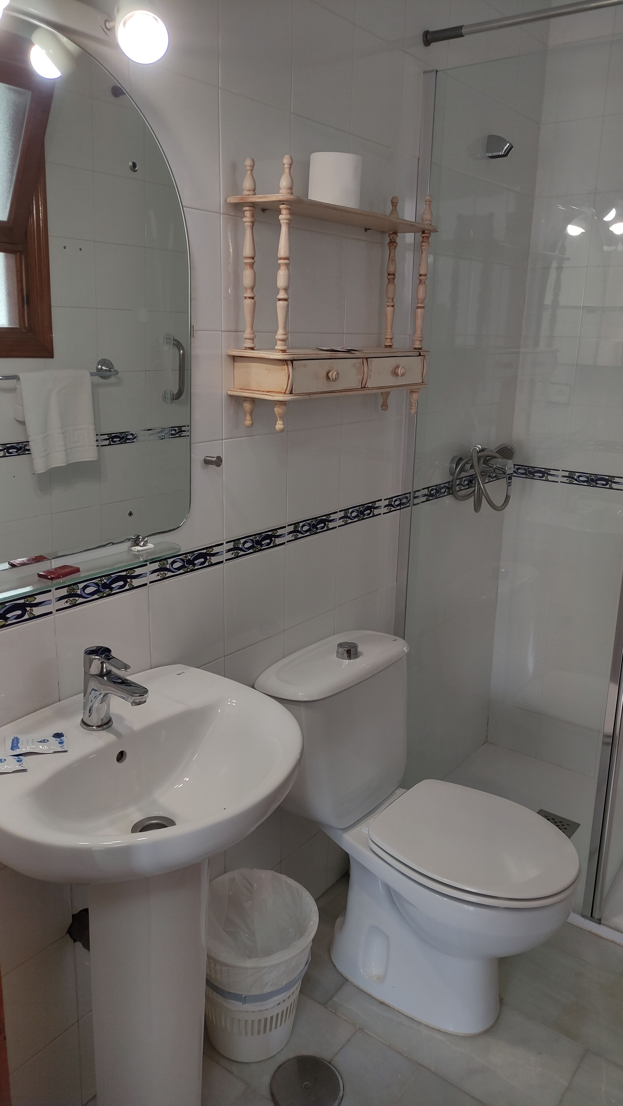 Une salle de bain équipée d’un lavabo, de toilettes et d’une douche. On y trouve un miroir, un porte-serviettes et un support à papier toilette.
