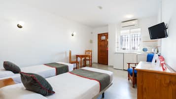 Une chambre d’hôtel avec deux lits, un bureau en bois, une chaise, une télévision et une kitchenette.