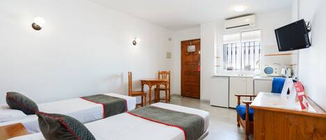 A hotel room with two beds, a wooden desk, a chair, a television, and a kitchenette.