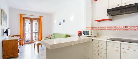 Una cocina con armarios blancos, microondas y una campana extractora roja.
