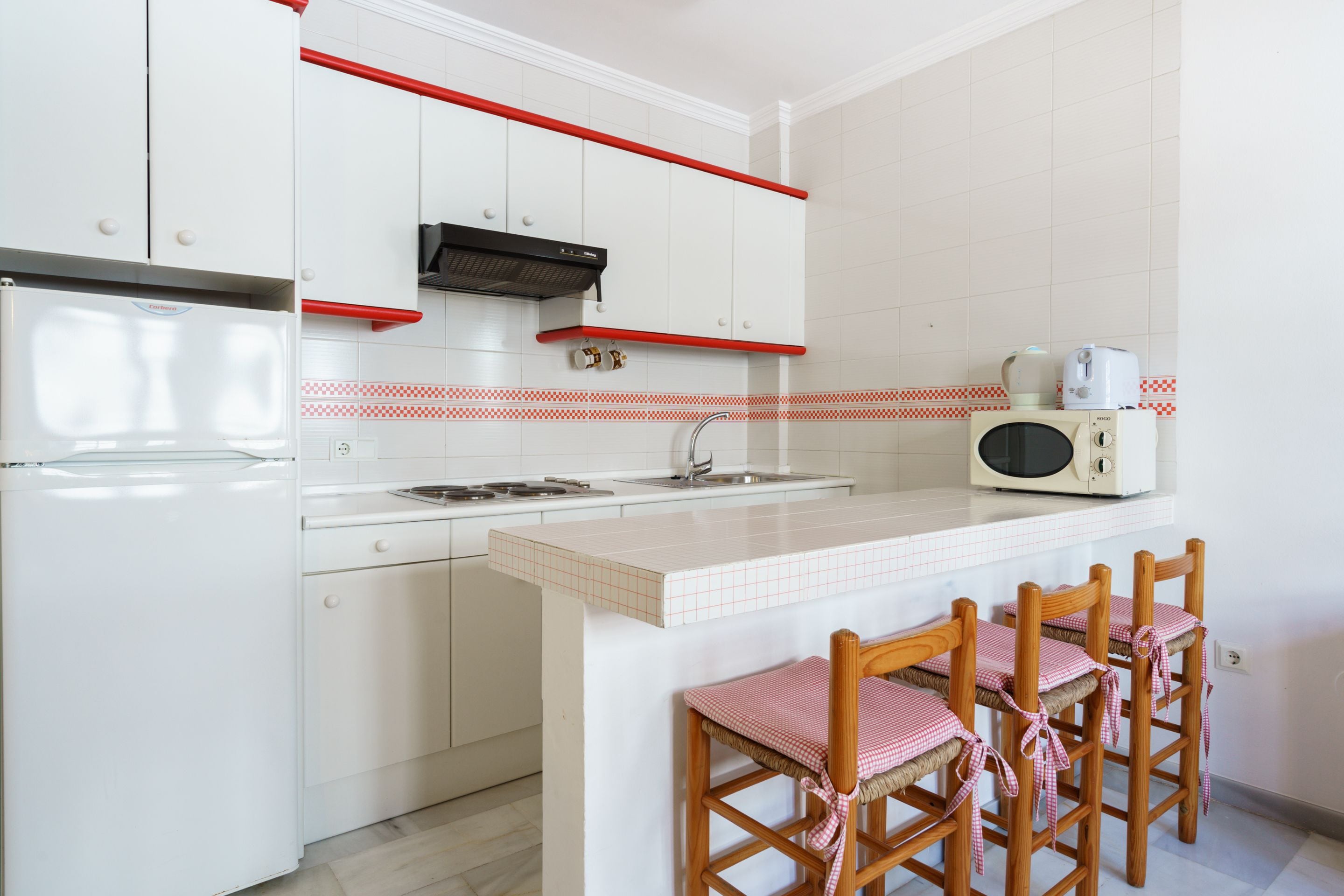 A kitchen with white cabinets, a microwave, and a red and white checkered backsplash.