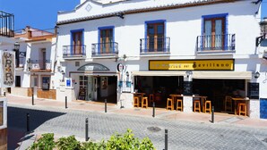 Un edificio blanco con contraventanas azules y balcones, que cuenta con un restaurante llamado "Los Hueritos Sevillano" y terraza.