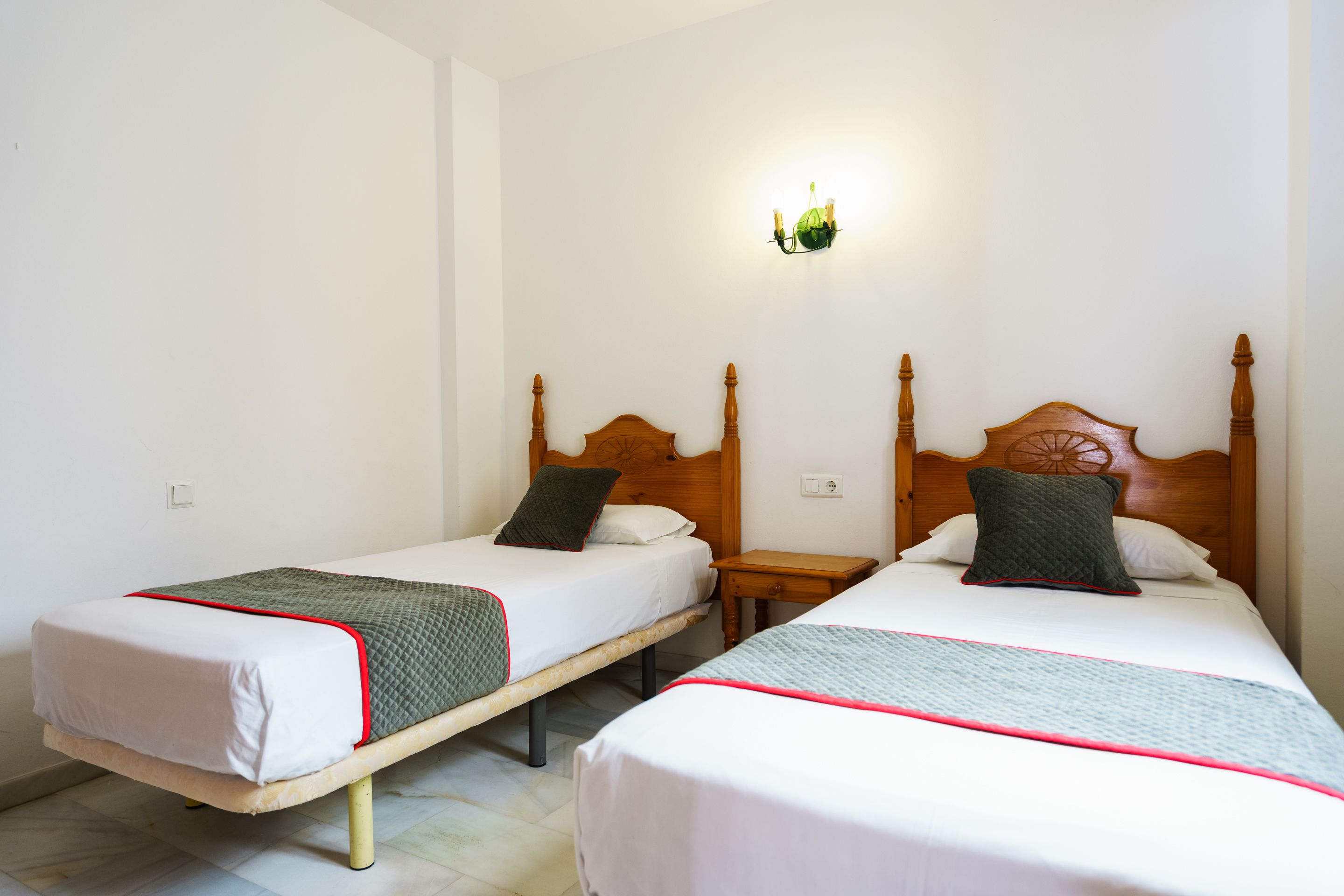 Two single beds with wooden headboards and nightstands, white bedding, and red trim.