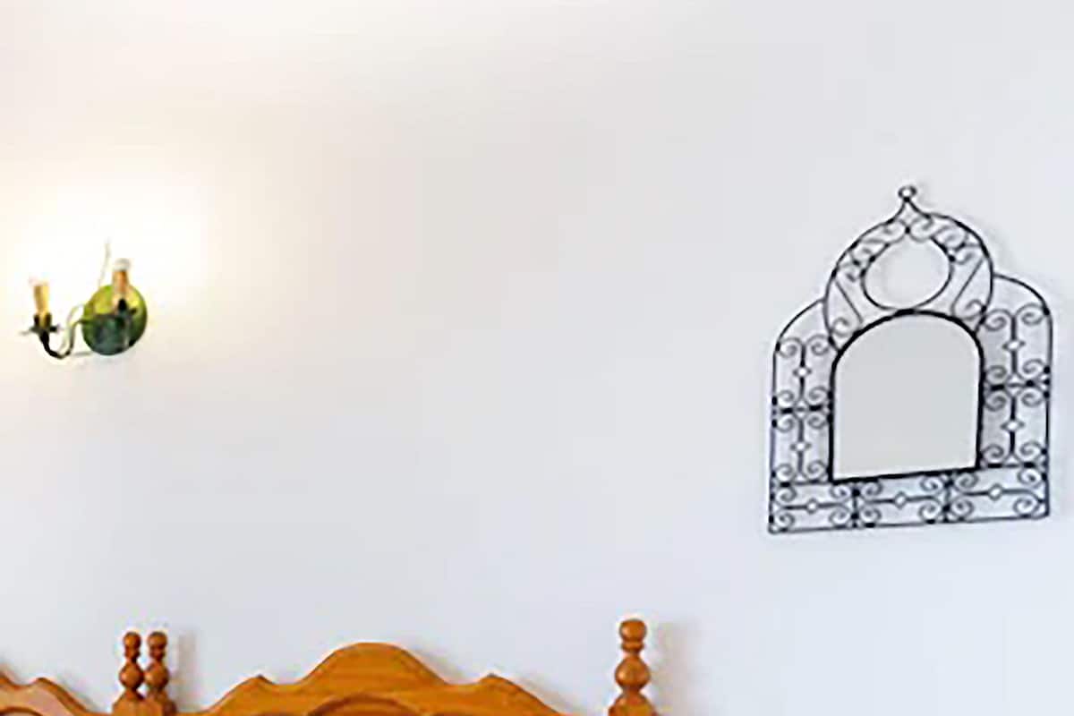 Een slaapkamer met een houten bed, een nachtkastje, een wandspiegel en een stopcontact.