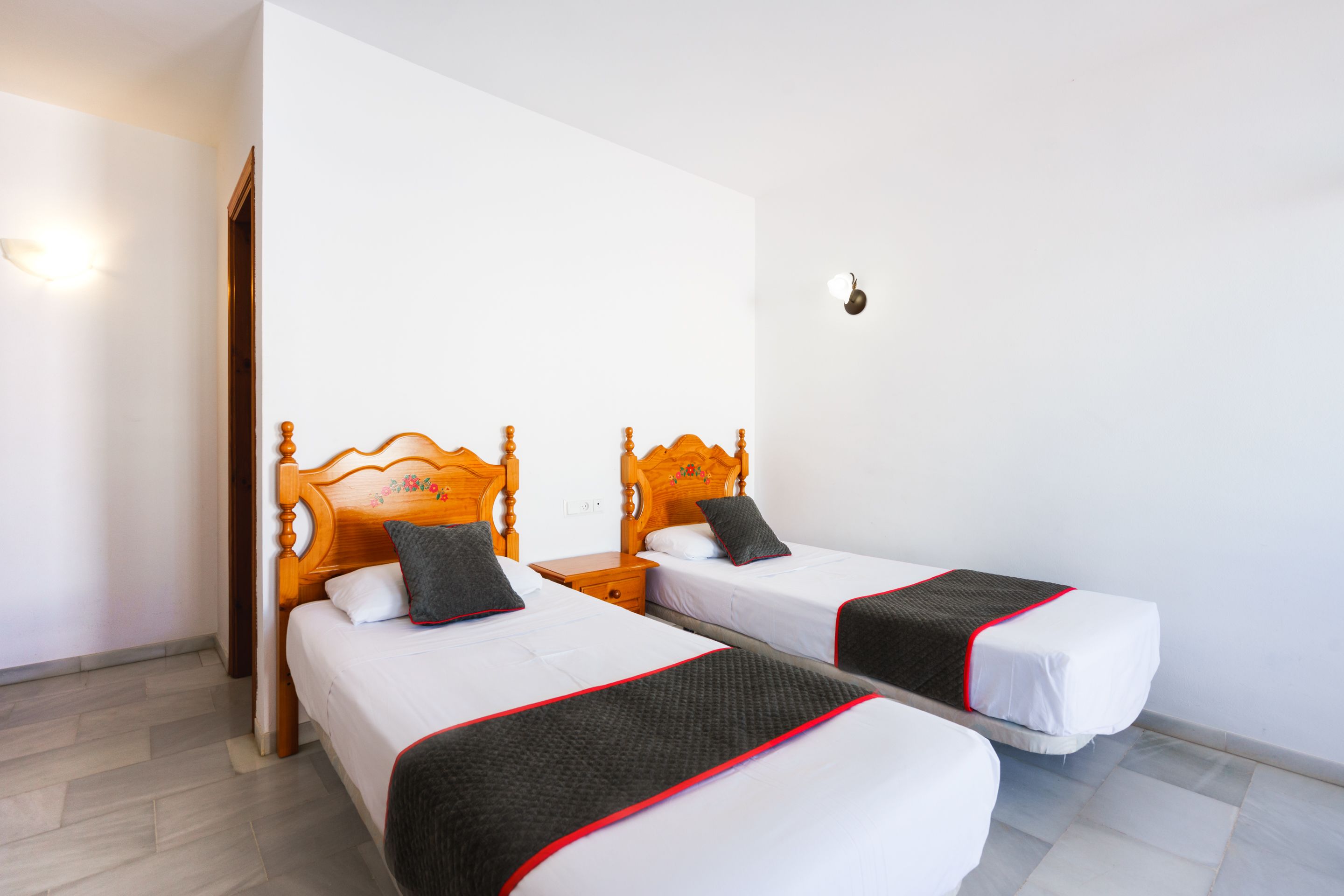 A hotel room with two wooden beds, white bedding, and a red trim.