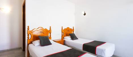 Une chambre d’hôtel avec deux lits en bois, du linge de lit blanc et des bordures rouges.