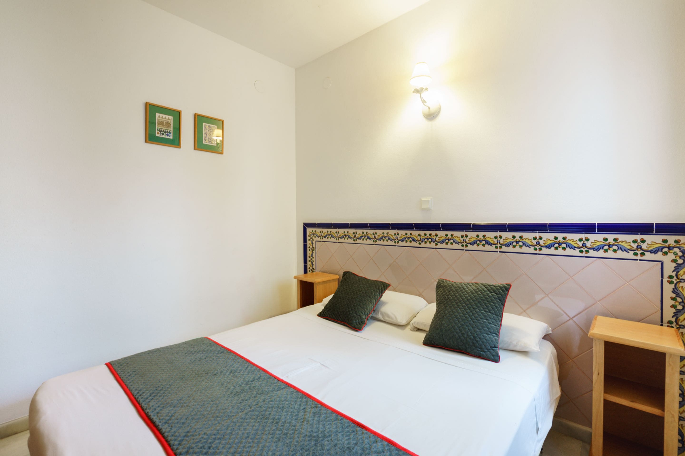 A neatly made bed with a white and green bedspread, two pillows, and a wooden nightstand beside it.