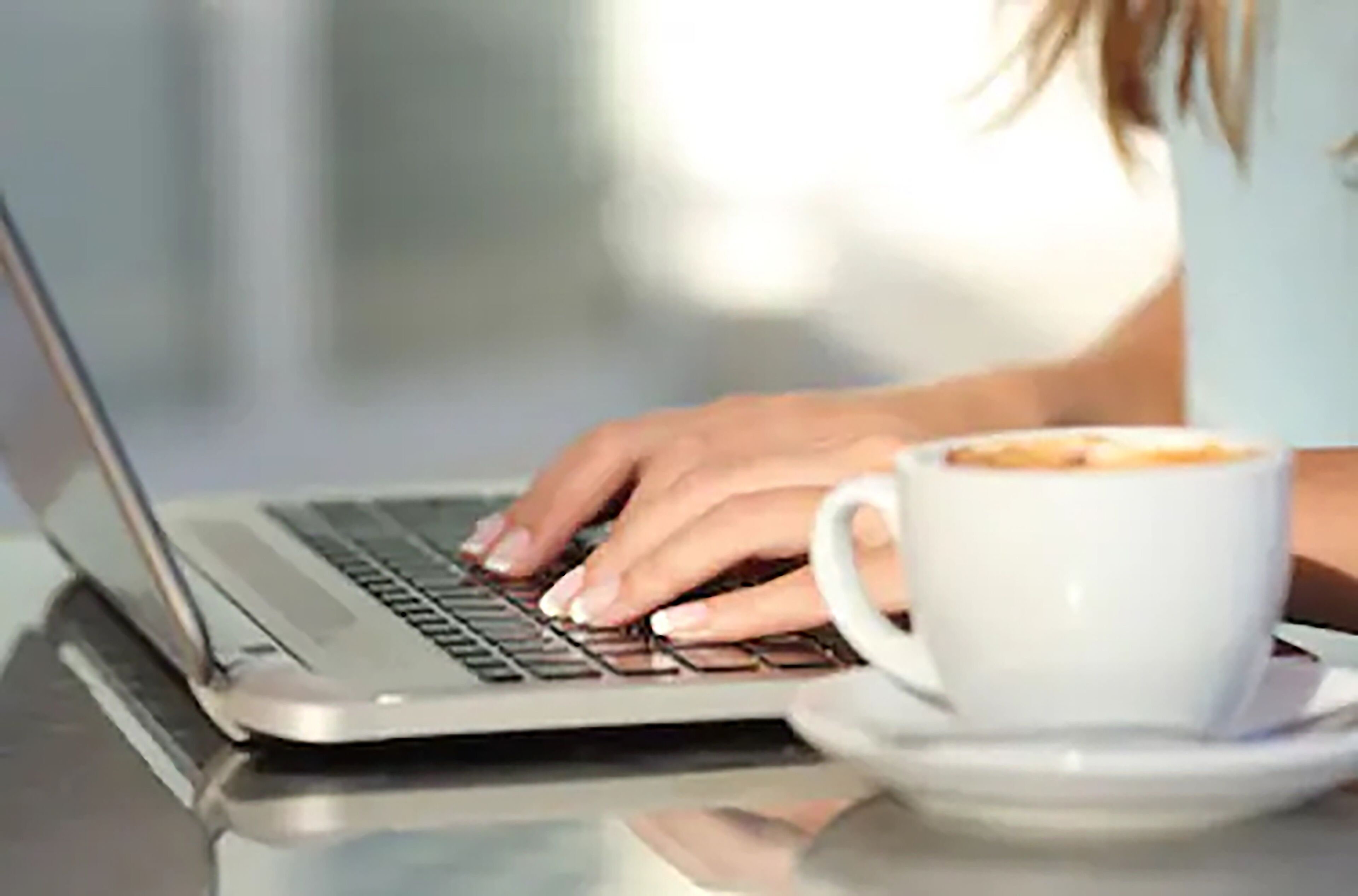 Una persona usando una computadora portátil sobre una mesa, con una taza de café.
